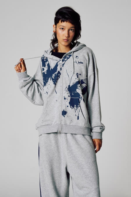 Veste grise Unwind, vue de l'arrière, avec capuche et pantalon de jogging coordonné à rayures bleu marine.