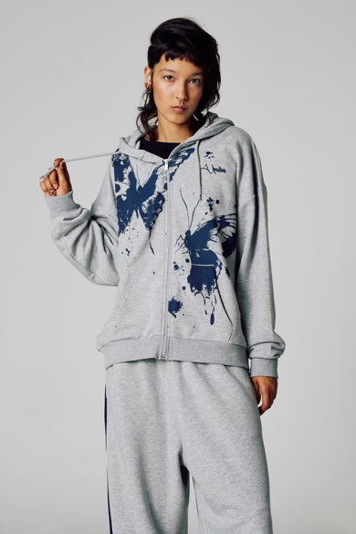Veste grise Unwind, vue de l'arrière, avec capuche et pantalon de jogging coordonné à rayures bleu marine.