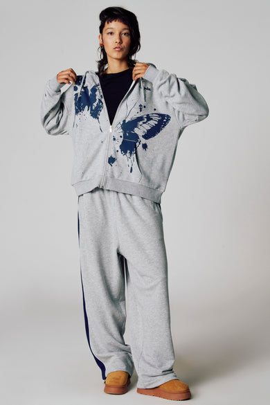 Veste grise Unwind, avec une imprimé de papillon et portée avec un haut noir et un pantalon de jogging gris.