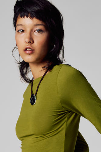 T-shirt vert avec manches longues d'Unwind, porté avec une chaîne et un cintre noir.