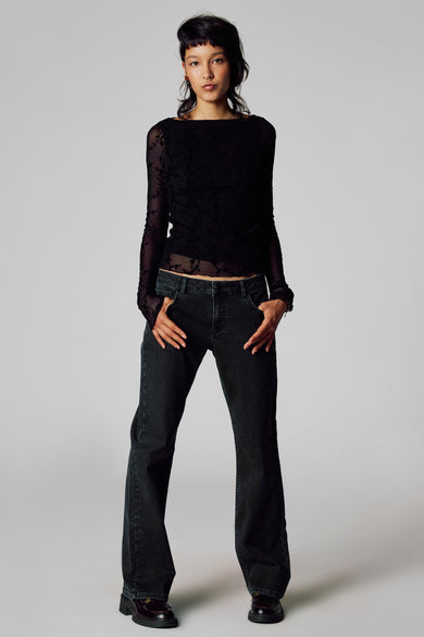 T-shirt noir à manches longues d'Unwind, avec un motif de fleurs et des manches transparentes, associé à un jeans foncé et des loafers en cuir.