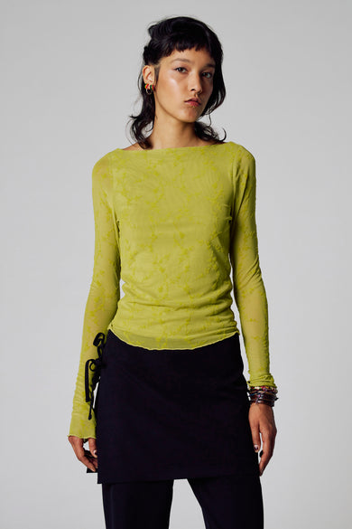 T-shirt vert avec manches longues d'Unwind, à motif et porté avec une jupe noire et des bracelets.