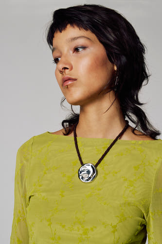 Robe verte à longues manches d'Unwind, avec un motif floral subtil et associée à une chaîne argentée.