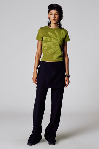 Pantalon noir d'Unwind, associé à un t-shirt vert olive avec motif floral et des mocassins noirs.