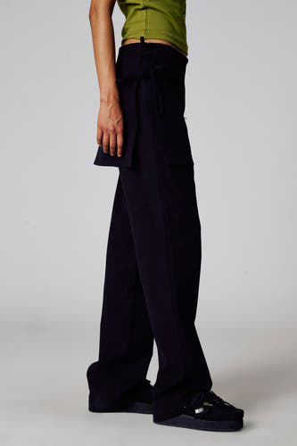 Pantalon noir Unwind, avec détail de ceinture et poche, associé à une chemise verte et des chaussures noires, en vue latérale.