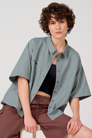 Chemise bleue à manches courtes d'Unwind, à motif à carreaux, portée avec un pantalon cargo marron.