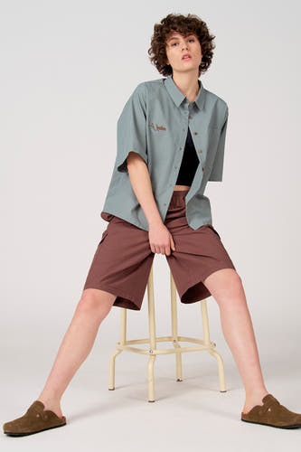 Chemise bleue à manches courtes d'Unwind, avec un petit motif à carreaux et un logo brodé marron.