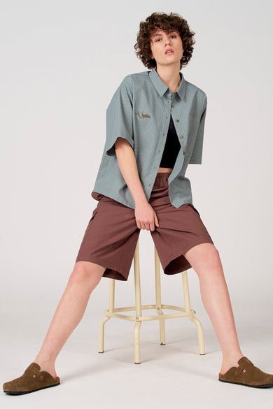 Chemise bleue à manches courtes d'Unwind, avec un petit motif à carreaux et un logo brodé marron.