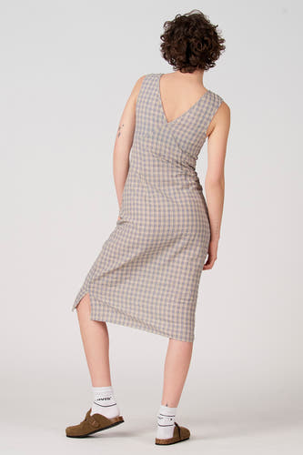 Robe sans manches bleue d'Unwind, avec un motif à carreaux et un col en V dans le dos, portée avec des chaussettes blanches et des mules marron.