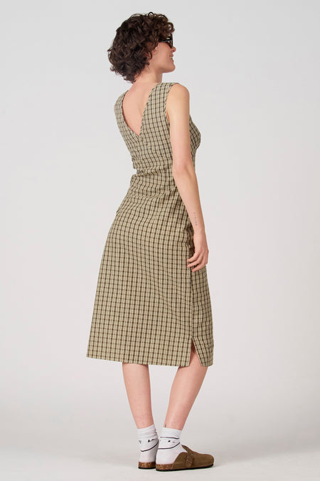 Groene mouwloze jurk van Unwind, met ruitpatroon en een split aan de zijkant, gedragen met witte sokken en bruine schoenen.
