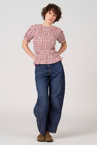 Chemisier rouge à manches courtes d'Unwind, à motif à carreaux, avec encolure élastique et coupe ample, porté avec un jean bleu.