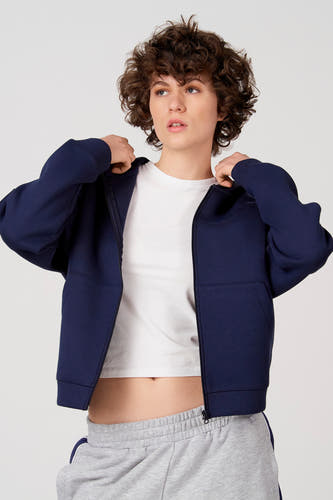 Gilet Unwind bleu, vu de dos, avec capuche et pantalon de jogging gris.