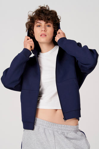 Gilet bleu d'Unwind, avec capuche et fermeture éclair, porté sur un t-shirt blanc et un jogging gris.