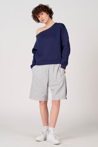 Blauwe sweater van Unwind, met blote schouder en gedragen met grijze shorts en witte sneakers.