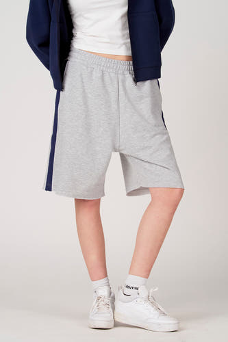 Short gris Unwind, avec une bande bleu foncé sur le côté et un bord effiloché, combiné avec des baskets et des chaussettes blanches.