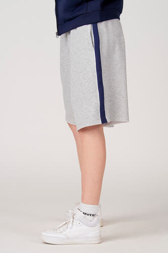 Grijze short van Unwind, met een donkerblauwe streep aan de zijkant en gerafelde rand, gecombineerd met witte sneakers en sokken.