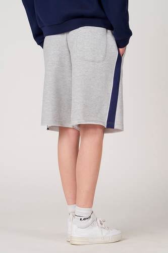 Short gris Unwind, avec une bande bleu foncé et blanche sur le côté, combiné avec des baskets et des chaussettes blanches.