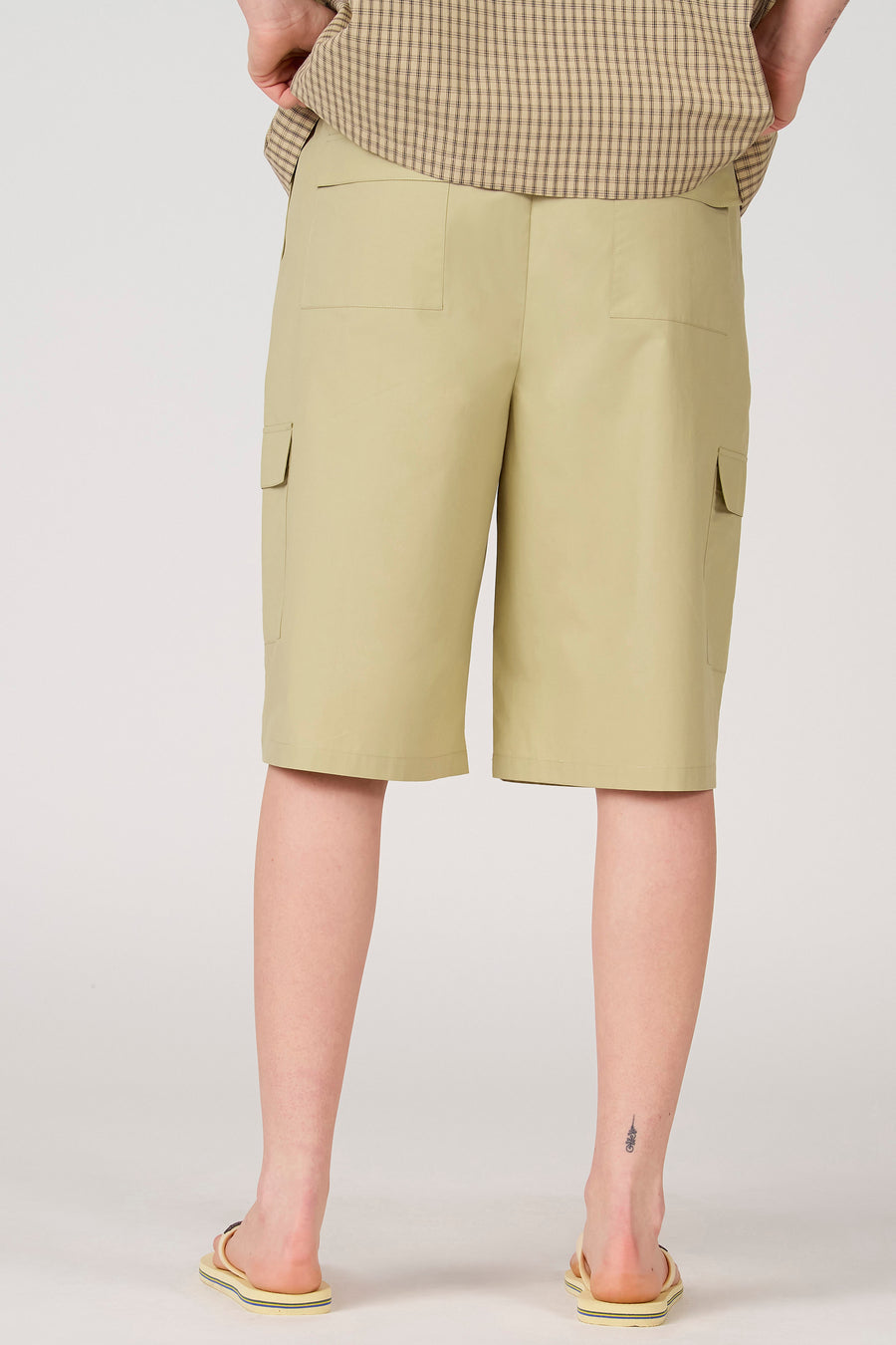 Lichtgroene short van Unwind met opgestikte achterzakken en cargozakken, gedragen met een geruit overhemd en slippers, achteraanzicht.