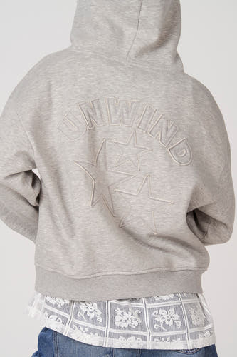 Sweat à capuche gris d'Unwind, avec texte brodé et étoiles dans le dos.
