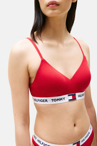 Sous-vêtement rouge de TOMMY JEANS avec une bande blanche et des détails de logo, porté par un modèle contre un fond uni.