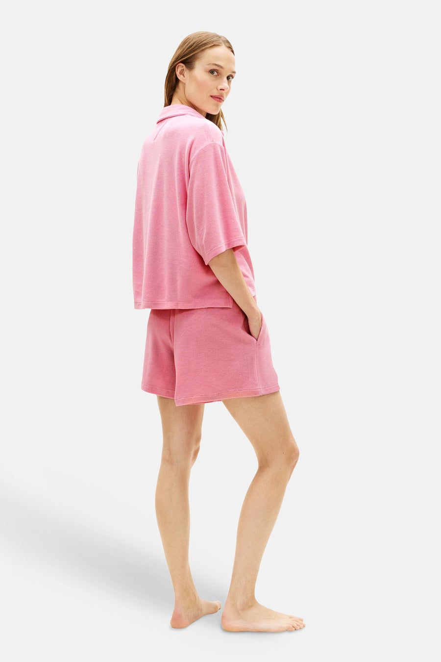 Polo rose à manches courtes de TOMMY JEANS, en tissu chiné, portée par un mannequin avec un short assorti.
