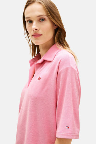 Polo rose à manches courtes de TOMMY JEANS, confectionnée en tissu éponge avec un logo FH brodé rouge et un logo drapeau sur la manche.