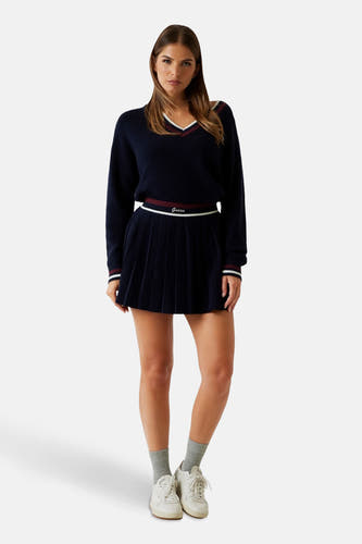 Jupe courte bleue de Guess, avec des plis et une ceinture avec le logo Guess, associée à un pull et des baskets.