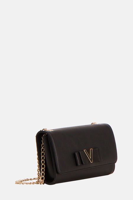 Sac à dos noir de VALENTINO BAGS, avec un logo V doré et une chaîne, tenu par une main dans un blazer blanc.