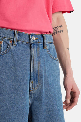 Short en jean bleu clair VANS "OFF THE WALL" avec bouton argenté, un t-shirt rose et un bras tatoué.