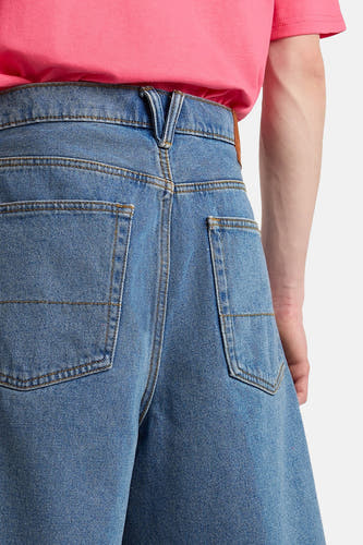 Short en jean bleu clair de VANS "OFF THE WALL" avec ceinture en forme de V, poches arrière plaquées et t-shirt rose, vue arrière.