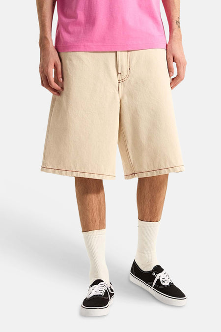 Ecru short van VANS met contrasterende bruine stiksels, gedragen met een roze T-shirt, crèmekleurige sokken en zwarte sneakers.