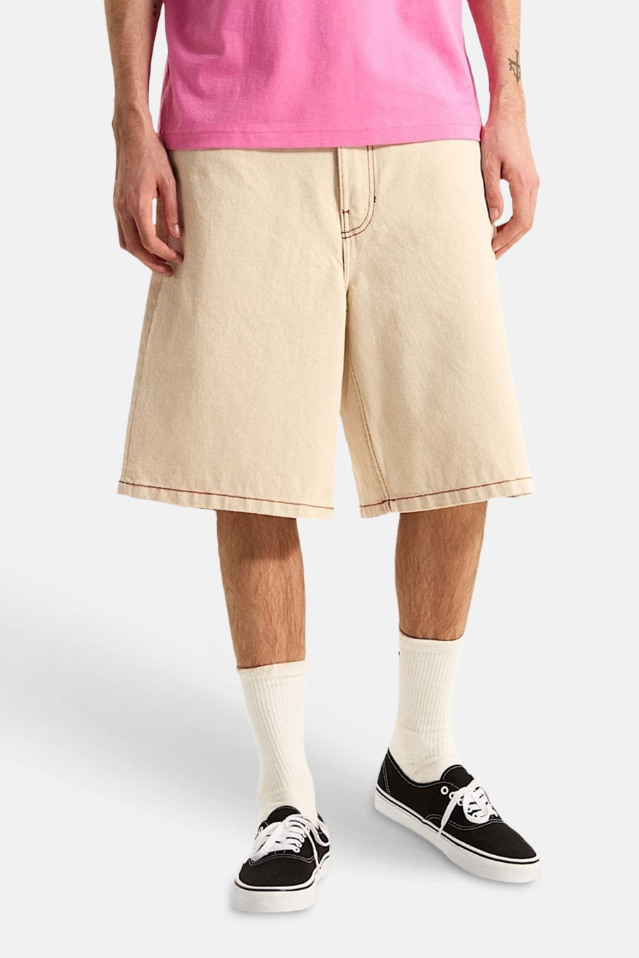 Ecru short van VANS met contrasterende bruine stiksels, gedragen met een roze T-shirt, crèmekleurige sokken en zwarte sneakers.
