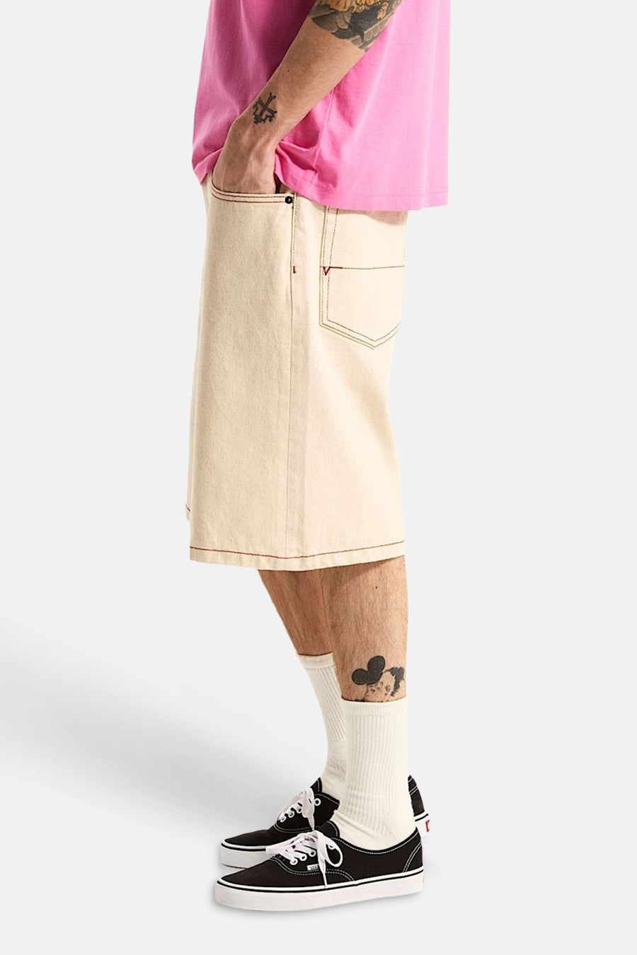 Ecru short van VANS “OFF THE WALL” met contrasterend roodbruin stiksel en V-vormige zakdetails, gedragen met roze T-shirt en sneakers.