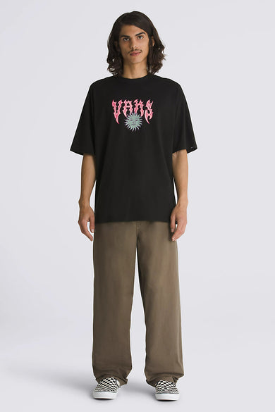 T-shirt à manches courtes noir de VANS, avec un logo flamme rose et un imprimé visage de soleil, porté avec un pantalon marron et des slip-ons à carreaux.