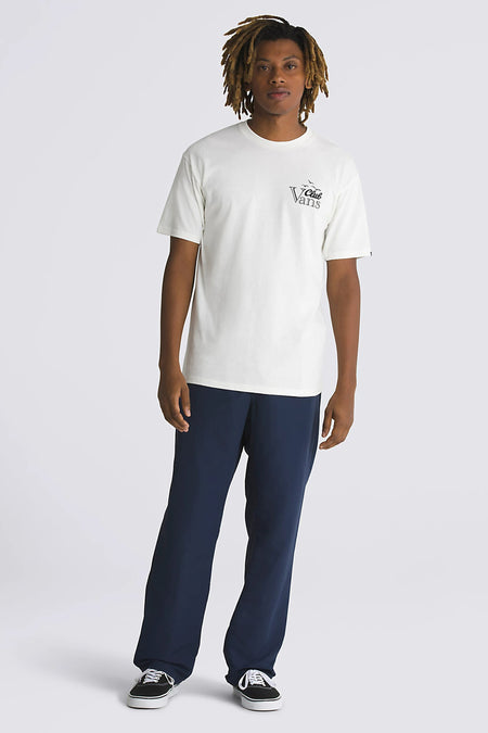 T-shirt écru à manches courtes de VANS, avec une petite impression sur la poitrine, porté avec un pantalon bleu et des chaussures noires.