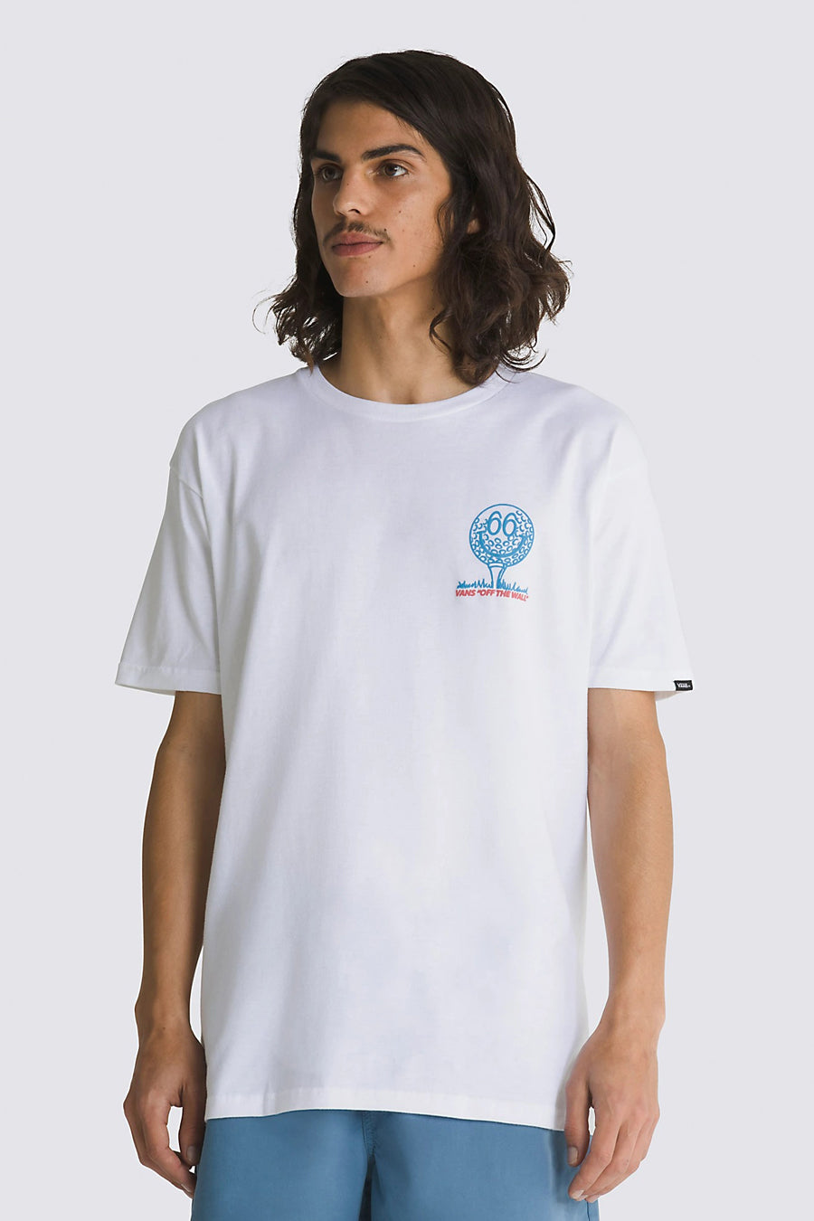 Man met lang haar, wit T-shirt met blauwe en rode print, blauwe korte broek.