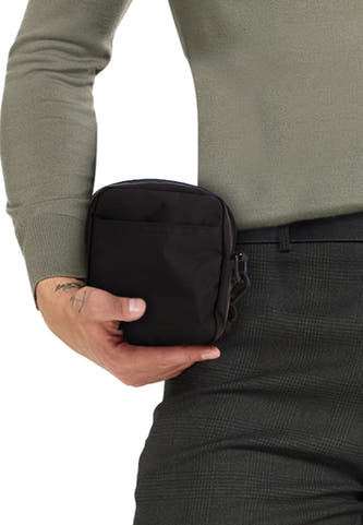 Sac à dos noir de VANS "OFF THE WALL", tenu par une personne en un pull vert et un pantalon kaki.