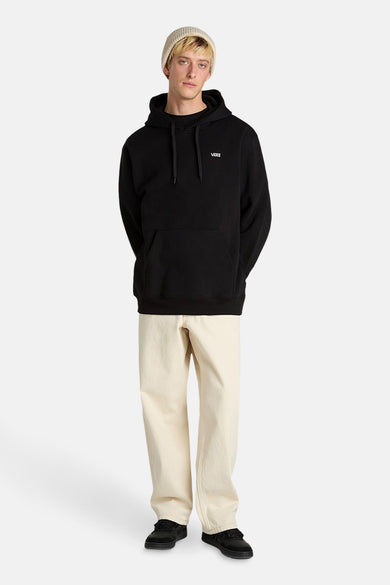 Pull-over noir avec capuche de Vans, porté avec un pantalon beige et des chaussures noires.