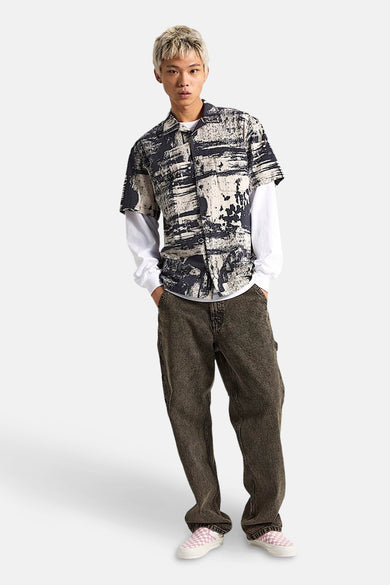 Chemise noire à manches courtes de VANS "OFF THE WALL" portée sur un chemisier blanc à manches longues.