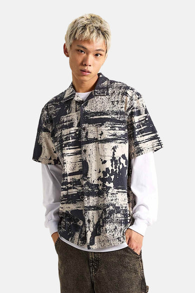 Chemise noire à manches courtes de VANS "OFF THE WALL", avec un motif abstrait noir et blanc, portée sur une chemise blanche.