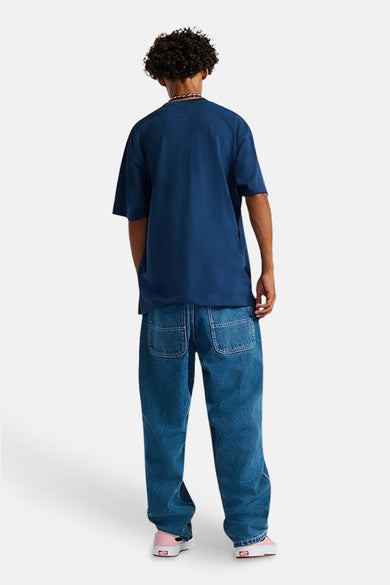 T-shirt bleu à manches courtes de VANS "OFF THE WALL", dos visible, associé à des jeans décontractés et des chaussures roses.