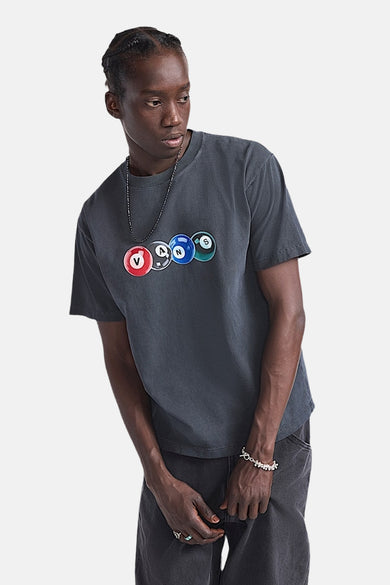 Man met grijze T-shirt met VANS-biljartballenprint, zwarte broek en zilveren sieraden.