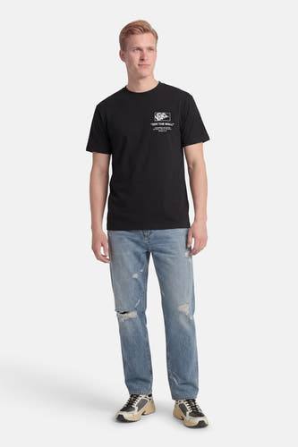Zwart T-shirt van VANS “OFF THE WALL”, gedragen met gescheurde jeans en sneakers.
