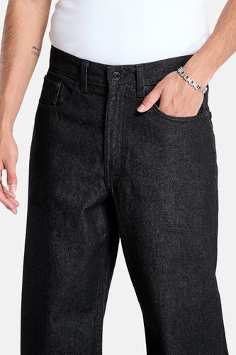 Jean droit noir de VANS "OFF THE WALL", avec un bracelet en argent et un t-shirt blanc.