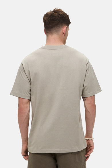 T-shirt beige à manches courtes de VANS "OFF THE WALL", vu par derrière, porté avec un bracelet en perles.