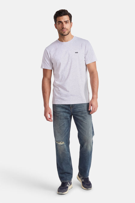 Grijs T-shirt van VANS “OFF THE WALL” met korte mouwen, gedragen met blauwe jeans met gaten en blauwe sneakers.
