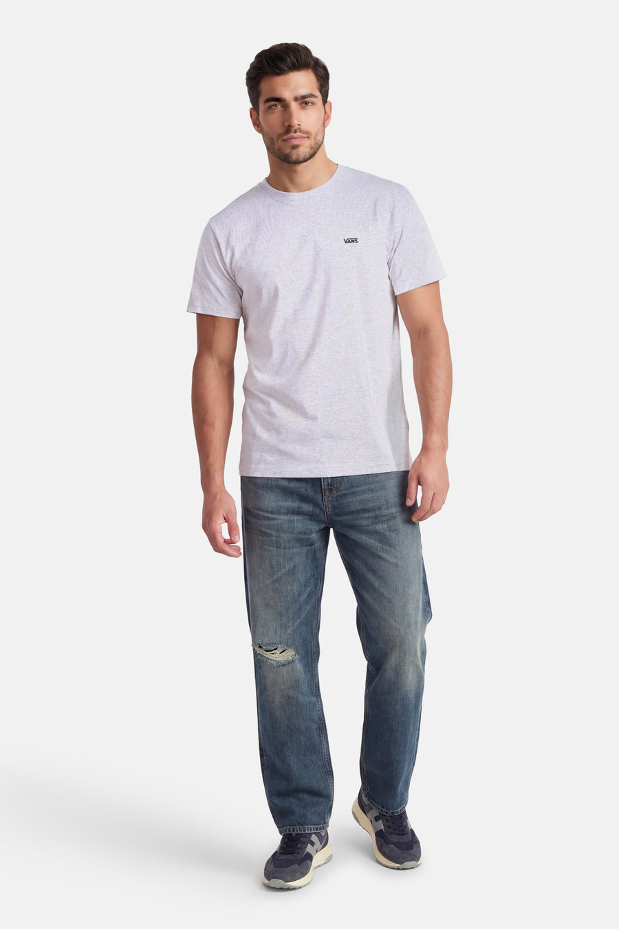 Grijs T-shirt van VANS “OFF THE WALL” met korte mouwen, gedragen met blauwe jeans met gaten en blauwe sneakers.
