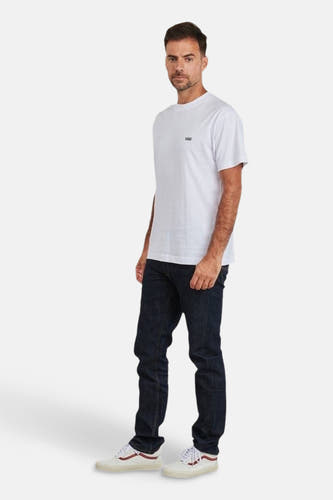 T-shirt blanc à manches courtes de VANS "OFF THE WALL", porté avec des jeans foncés et des baskets basses.