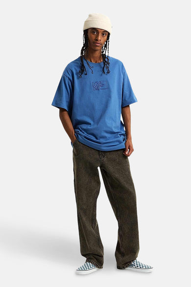 T-shirt bleu à manches courtes de Vans avec logo sur la poitrine, porté avec une casquette crème et un pantalon foncé.