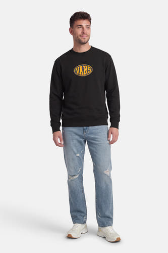 Zwarte sweater van VANS “OFF THE WALL” met geel logo op de borst, gecombineerd met een blauwe jeans en witte sneakers.

